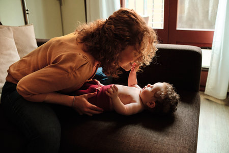 Woman changing her daughters clothes on the sofa at home.