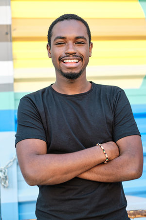 Confident man smiling while standing with crossed arms outdoors.の写真素材