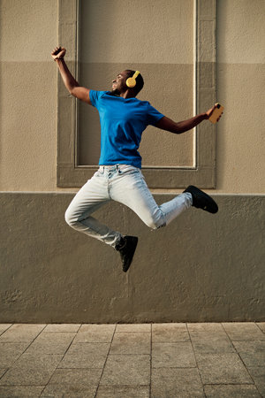 Excited man jumping while listening music with headphones and mobile phone outdoors.