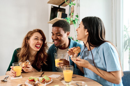 Multiethnic friends eating pastries sitting at homeの写真素材