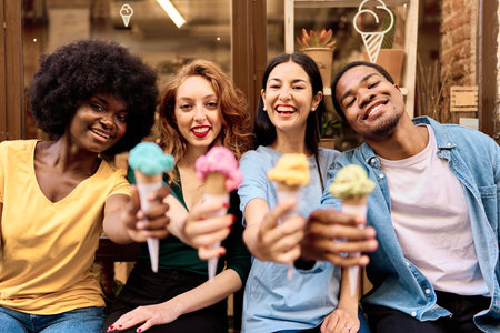 Smiley multiracial friends raising cones of ice-cream outdoorsの写真素材