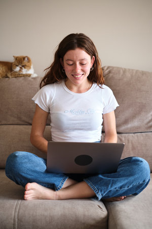 Smiling woman using laptop on the sofa with a cat