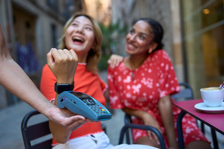 Cheerful lesbian couple paying the coffee with smart watchの写真素材