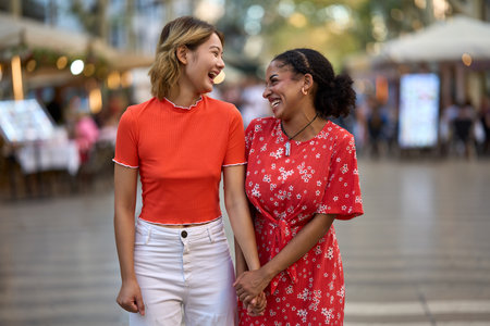 Multicultural lesbian couple holding hands walking along the cityの写真素材