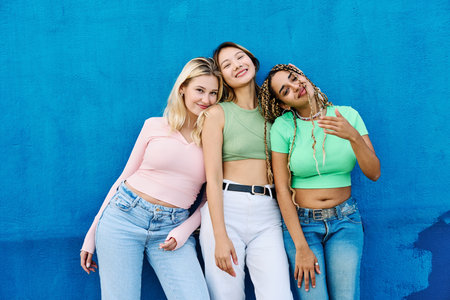 Three multi-ethnic women posing smiling on a blue wallの写真素材