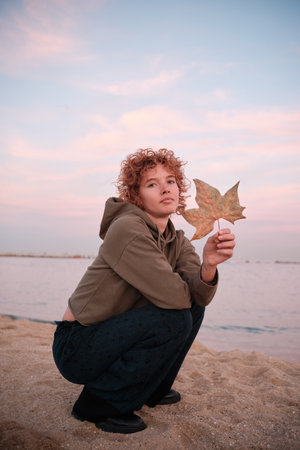 Woman holding autumn leaf at sunset beachの写真素材
