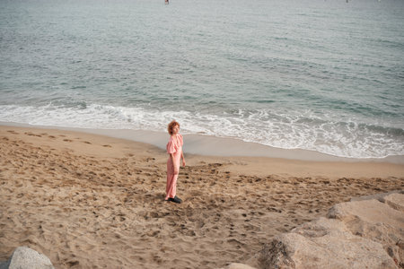 Woman in pink dress walking along beach looking backの写真素材