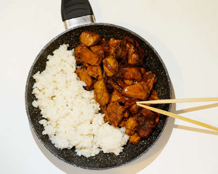 Korean grilled chicken with white rice and Asian Chopsticks in frying pan on brown napkin and white...