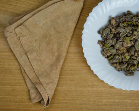 Habas a la Catalana, stew of beans in a white dish with a brown napkin on a wooden table. Top view