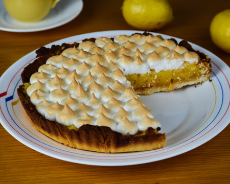 Lemon Pie with meringue without one slice in a dish decorated with two lemons and a cup of coffee