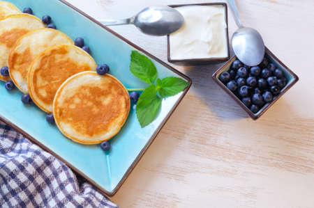 Pancakes with blueberry in rectangular plate and bowls with sour and berries on the wooden background. Overhead viewの写真素材