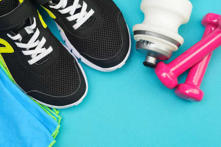 Pink dumbbells, sport bottle, towel and black running shoes on the sport mat