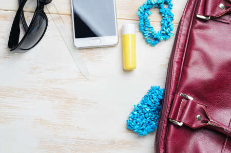 Woman's bag and it's content - phone, lipstick, sunglasses, nail file, necklace