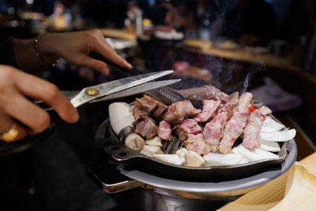 Authentic Korean BBQ Experience, Hands Cutting Meat on Grillの写真素材