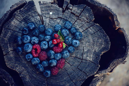 Heart laid out of blueberries and raspberries on an old wooden backgroundの写真素材