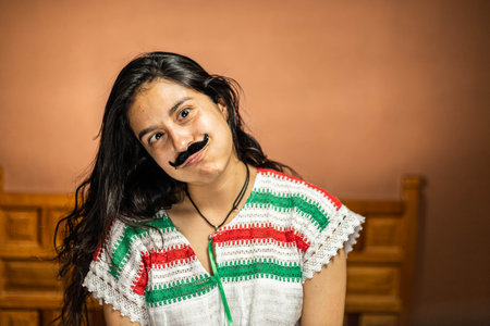 Mexican woman dressed in clothes of the patriotic colors with a fake mustache, making funny facesの写真素材