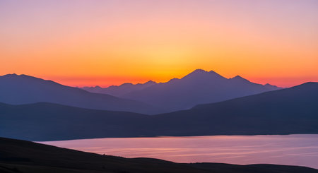 Lake showing mountain range silhouetted against a vibrant orange and purple sunset sky over a...