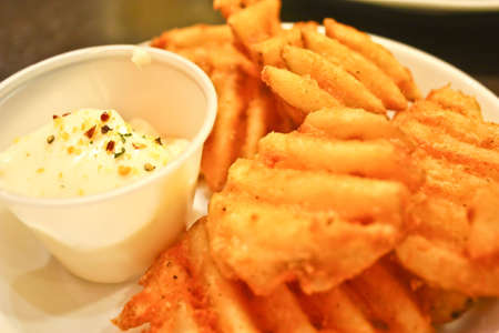Freshly fries waffle fries served with tartar sauce on a plateの写真素材