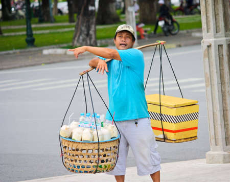 Ho Chi Minh City, Vietnam - June 10, 2010 - A Vietnamese drink stall owner carries drinks and points out direction to visitors.のeditorial素材