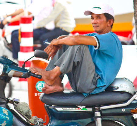 Ho Chi Minh City, Vietnam - June 10, 2010 - A tired Vietnamese man sitting down on his bike and having a smoke on Ho Chi Minh City, Vietnamのeditorial素材