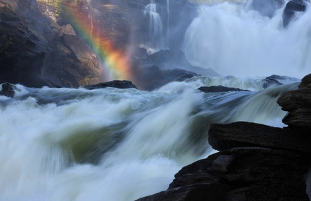 Raging river creates rainbow when steam meets sunlight.の写真素材