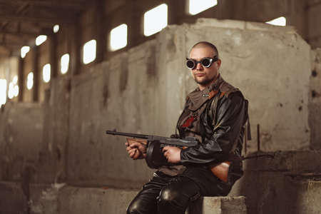 Portrait of a man from post-apocalyptic world with submachine gun and the black glasses in an...