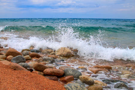 Water wave splashes, against a clear blue sky background. A beautiful blue mountain lake with round stones on the shore. Summer, tourism. Pure blue water, clear sky, water splashes, waves.の写真素材