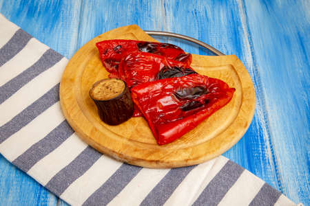 Baked vegetables - red bell pepper and eggplant on a wooden round board. On a rustic blue wooden table.の写真素材
