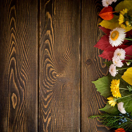 Autumn background. Bright orange berries, very flowers and leaves on a brown wood background. Background for autumn holidays and thanksgiving day.の写真素材