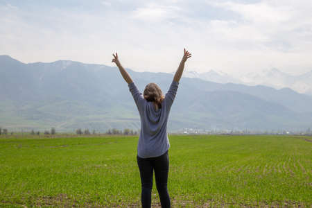 Young beautiful girl in nature. Good mood on a bright spring day. Green fields and blue mountains.