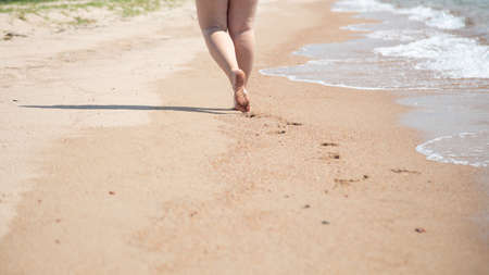 Closeup of bare feet on the beach. Walking on the sand at the water's edge. Vacation and travel concept. Cosmetics and body care.の写真素材