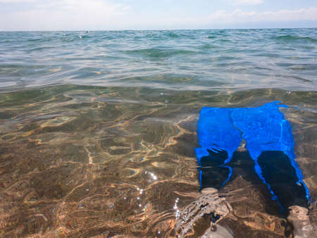 Texture of transparent water with sandy bottom and blue sky. Legs in flippers.