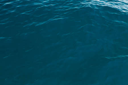 Clear water texture in blue. Background of the ocean and the sea backlit by the sun. Natural water
