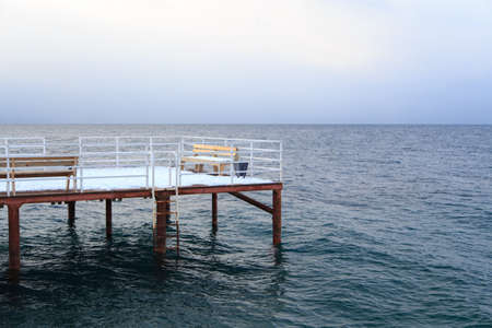 Winter beach. Blue clear sea water, snow and a wooden pier. Skyline and mountains. Kyrgyzstan, Issyk-Kul Lakeの写真素材