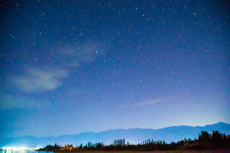 Starry sky and clouds. Night landscape, lights reflecting in the sea and mountains. Natural...