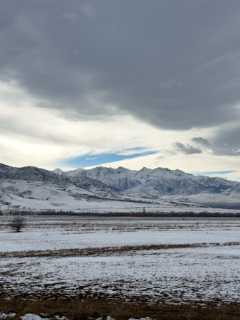 Snow covered mountains in Kyrgyzstan under cloudy winter sky peaceful rural landscape.