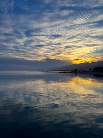 Quiet mountain lake, evening light on the water, Kyrgyzstan. Still water and mountain reflection in the lake. Sunset over Issyk-Kul with reflections in calm waterの写真素材