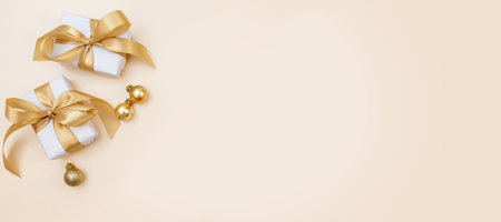 Stylish winter layout with white presents, gold bows and sparkling ornaments on beige background. Perfect for greeting cards, web banners or branding.の写真素材