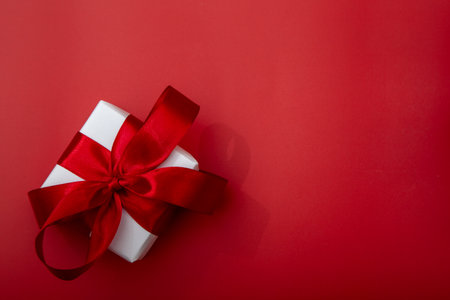 White luxury gift box with satin red ribbon on elegant red background. Sophisticated composition for jewelry and premium gift brandingの写真素材