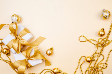 Stylish winter layout with white presents, gold bows and sparkling ornaments on beige background. Perfect for greeting cards, web banners or branding.の写真素材