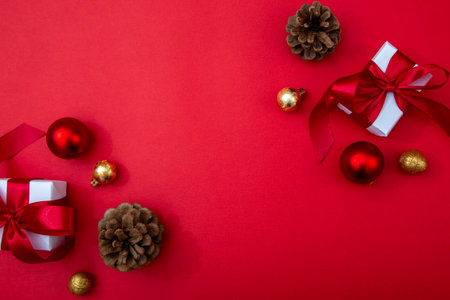 Christmas composition with gifts, baubles and pinecones on red background. Festive copy space backdrop for greetings and advertisingの写真素材