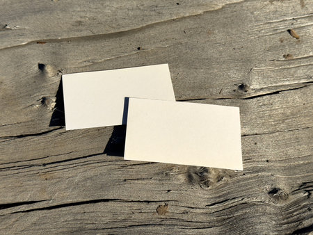 Two blank business cards placed on aged wooden surface. Warm sunlight creates natural atmospheric mockup for branding presentation.の写真素材