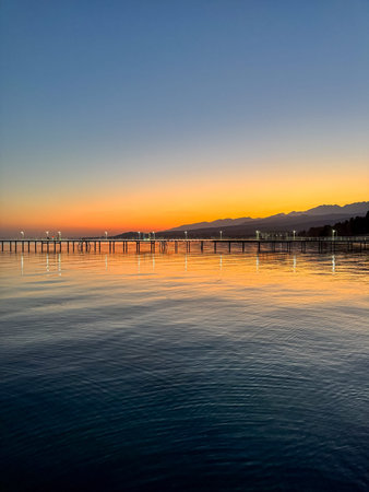 Evening sunset at Issyk Kul Lake in Kyrgyzstan. Long illuminated pier stretching into calm water...