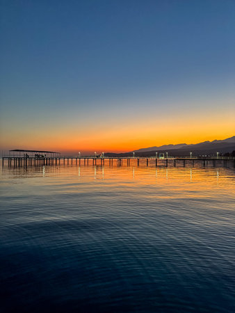 Evening sunset at Issyk Kul Lake in Kyrgyzstan. Long illuminated pier stretching into calm water...