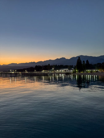 Evening sunset at Issyk Kul Lake in Kyrgyzstan. Long illuminated pier stretching into calm water...