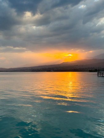 Scenic sunset over Issyk Kul Lake in Kyrgyzstan. The sun sets behind the mountains, casting a golden reflection across the water. Sunset over Issyk Kul Lake in Kyrgyzstan with golden reflection on the water.の写真素材