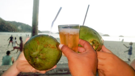 three hand holding coconuts and glass of beer on the beach on a summer afternoon in rio de janeiro brazilの写真素材