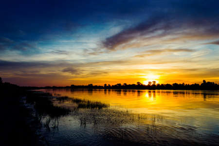 River at sunset and silhouettes of the bushes on the opposite bankの写真素材