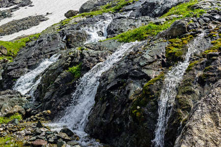 A fast mountain stream with a waterfall flowing over stones closeupの写真素材