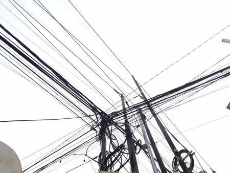 Chaotic overhead power lines and utility poles forming an abstract urban network against a bright...